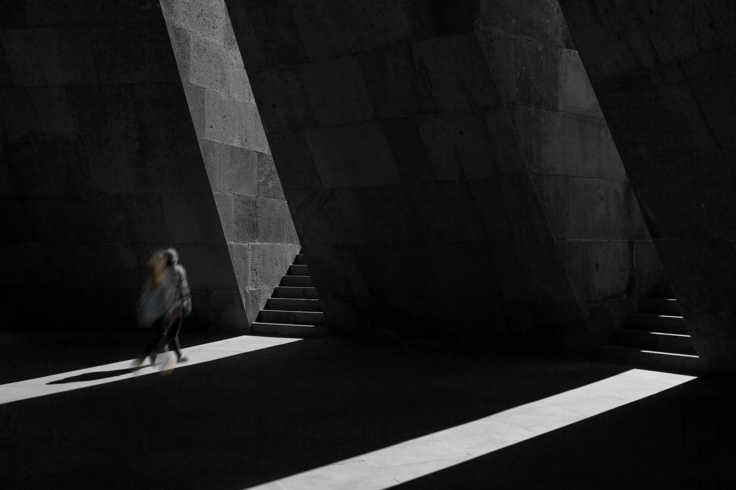 Editorial study of a figure moving through a concrete passage toward the light.